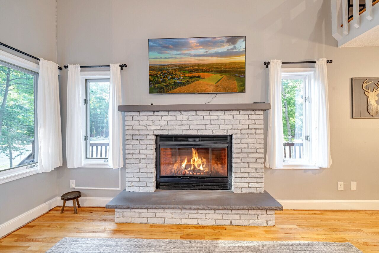 A room with a fireplace, large windows, and a painting on the wall.