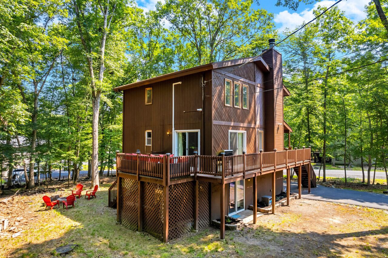 A two-story wooden cabin with a deck, surrounded by trees.