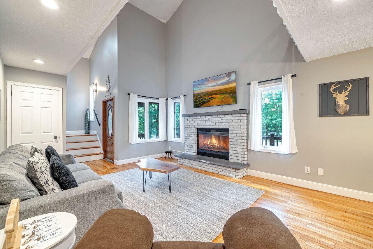 Un salón amplio con chimenea, un sofá, una mesa de centro y una escalera que lleva a un nivel superior.
