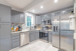 A modern kitchen with grey cabinetry, stainless steel appliances, and a tiled backsplash.