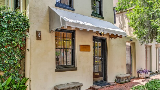 A building with a white awning, a black door, and a window with metal bars. - Enchanted property with a beautiful courtyard! (Savannah)
