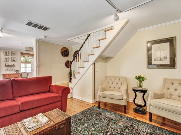 A living room with a red sofa, two beige armchairs, a patterned rug, and a staircase with white railings.