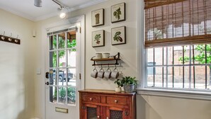 A wooden door with glass panels, a small cabinet with decorative items, and a window with blinds. - Enchanted property with a beautiful courtyard! (Savannah)