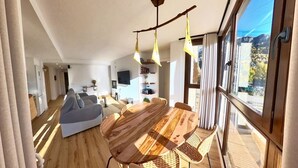 Un salon moderne avec une table à manger en bois, un canapé gris et un téléviseur fixé au mur.