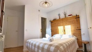 Une chambre à coucher avec une tête de lit en bois, un lit recouvert d’une couverture à carreaux, une petite table de chevet et un luminaire fixé au plafond.