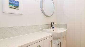 Une salle de bain avec un meuble-lavabo blanc, un lavabo avec un robinet, un miroir et des toilettes.