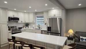 A modern kitchen with white cabinetry, a stainless steel refrigerator, and a central island with bar stools. - Fully renovated private & cozy 3 bdr cottage with hot tub close to Warren Dunes  (Sawyer)