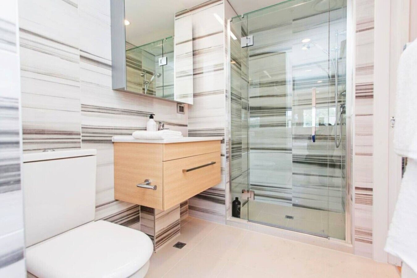 A modern bathroom with a toilet, vanity, and glass shower enclosure.