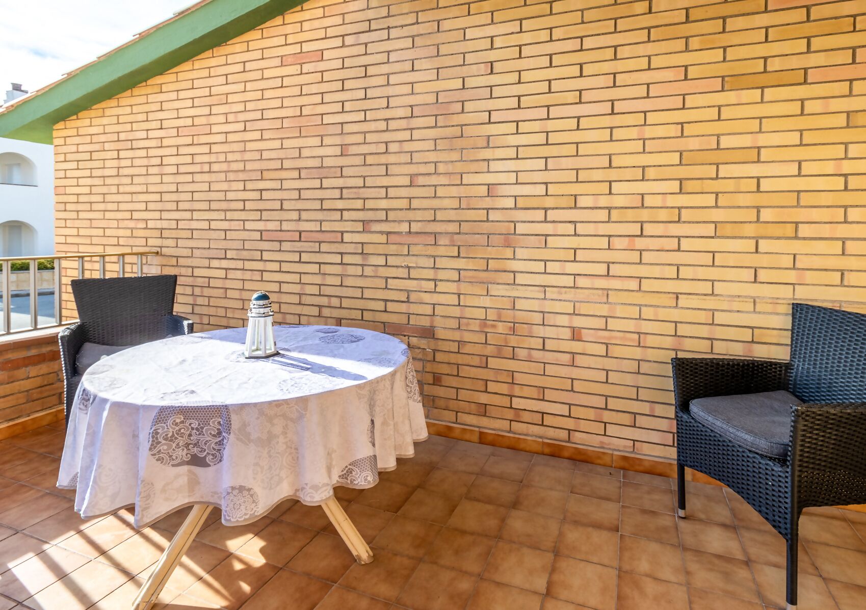 A patio with a round table covered by a white lace tablecloth, two wicker chairs, and a decorative salt shaker.