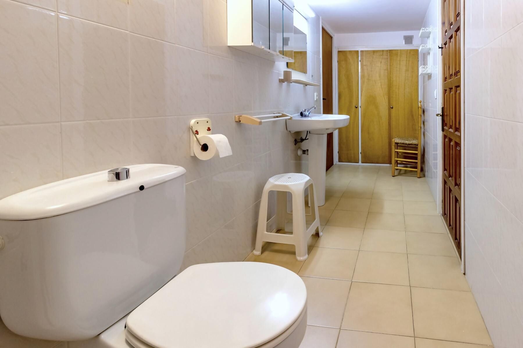 Een badkamer met toilet, wastafel en een klein krukje.