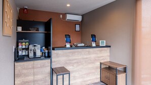 Uma área de recepção moderna com balcão de madeira, máquina de café e quiosque digital.