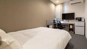 Quarto de hotel com uma cama grande, uma escrivaninha com computador, televisão, micro-ondas e frigorífico.