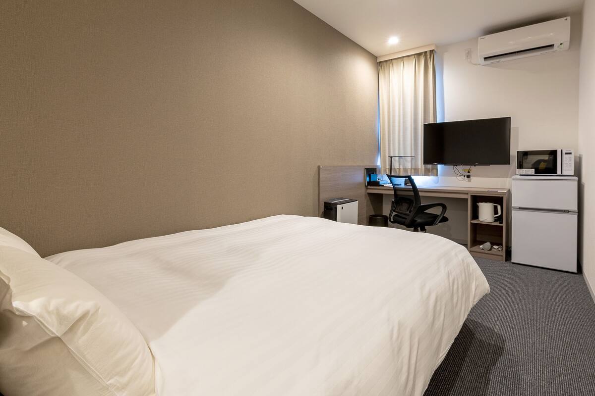 A hotel room with a large bed, a desk with a computer, a television, a microwave, and a refrigerator.