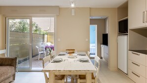 A compact kitchen with a dining table set for four, a TV mounted on the wall, and a sliding glass door leading to an outdoor area with chairs.