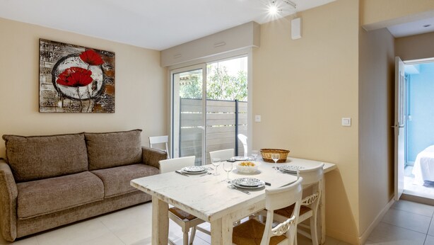 A dining area with a white table and chairs, a brown couch, and a painting with red flowers.