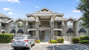 A multi-story building with a central entrance, stone pillars, and a parking lot with a parked car. - Family-Friendly 3BR Retreat • Golf Course Views + Ticket Discounts (Branson)