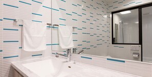 Une salle de bain moderne avec des carreaux blancs et des touches de bleu, un grand miroir et un lavabo doté d’un robinet chromé.