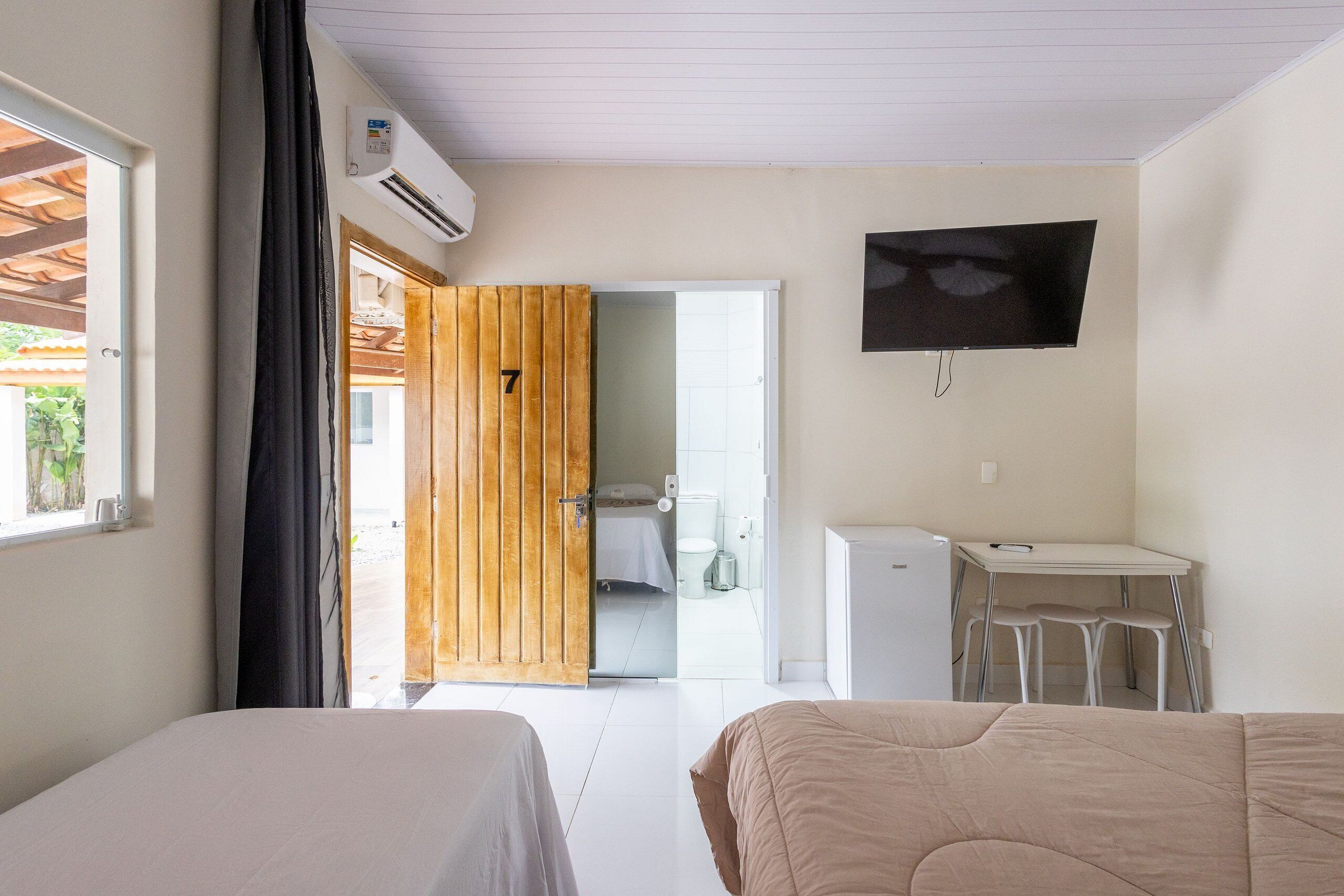 Habitación de hotel con dos camas, un escritorio, un televisor y un baño visible a través de una puerta abierta.