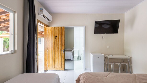 A hotel room with two beds, a desk, a TV, and a bathroom visible through an open door. - Maresias Suítes (São Sebastião)