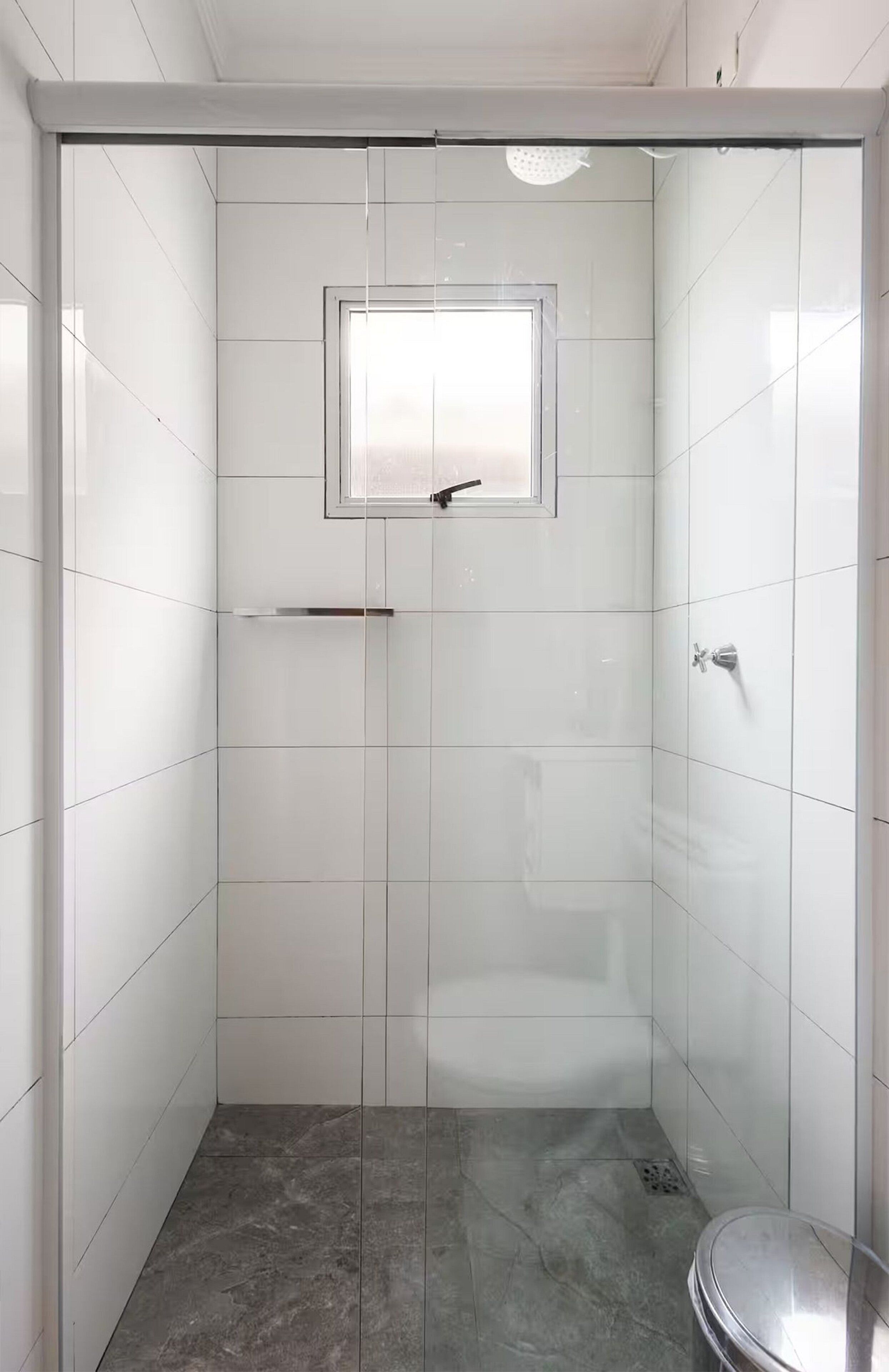 A walk-in shower with a glass door, a small window, and a showerhead.