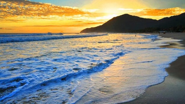 A beach with waves and a sunset. - Maresias Suítes (São Sebastião)