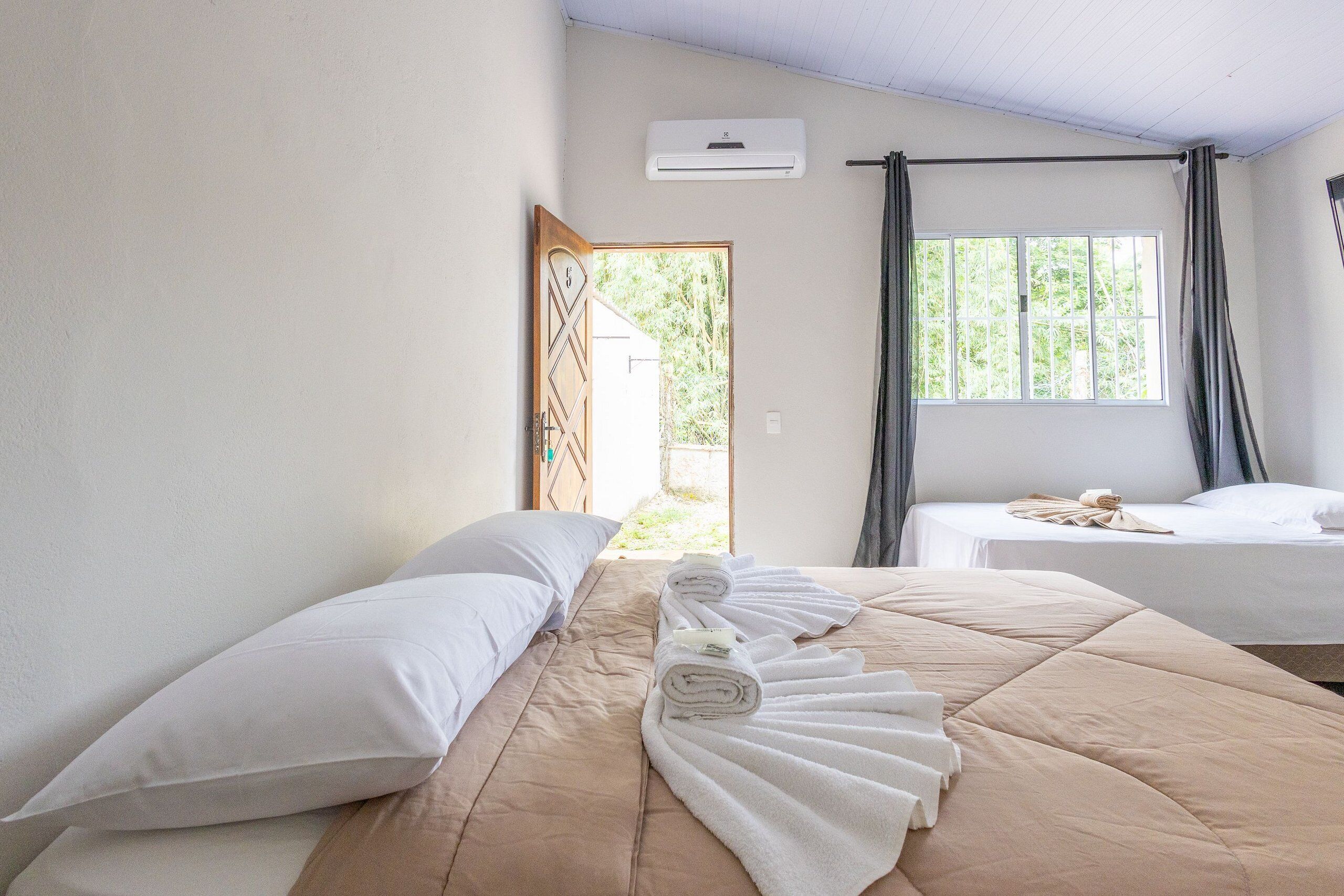 A hotel room with two beds, a window with curtains, an air conditioning unit, and a door leading outside.
