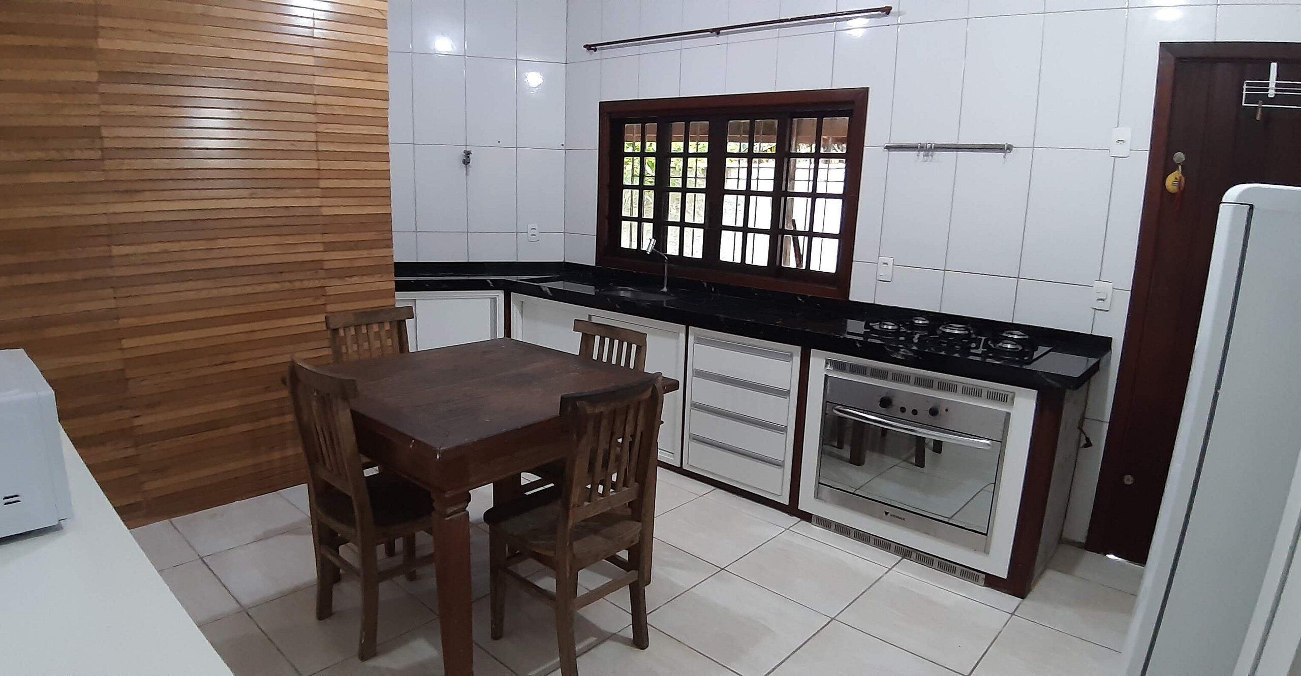 A kitchen with a wooden table and chairs, a window with a grid pattern, white cabinets, and a built-in oven.