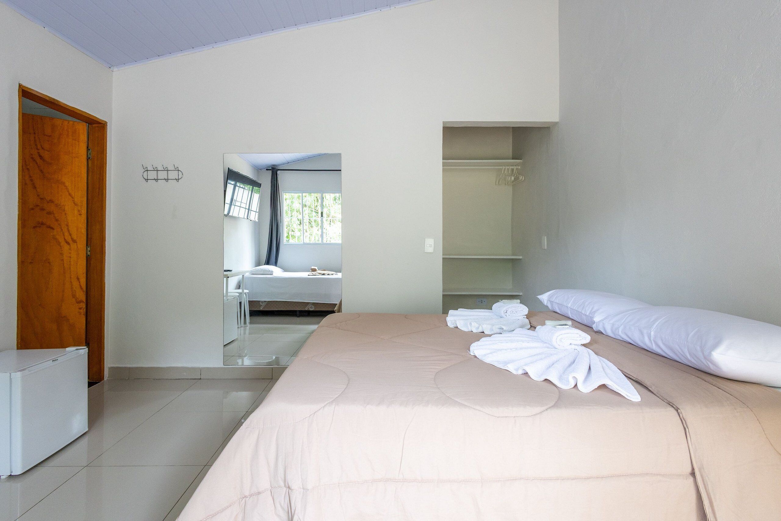 Quarto de hotel com cama, guarda-roupa, espelho e janela.
