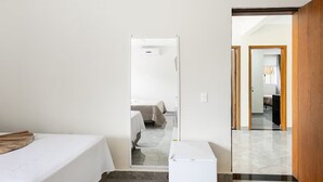 A hotel room with a bed, a small table, and a door leading to another room. - Maresias Suítes (São Sebastião)