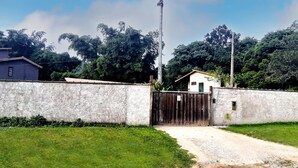 A gated compound with a dirt path leading to a building with a corrugated metal roof. - Maresias Suítes (São Sebastião)