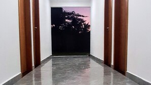 A hallway with a polished marble floor, white walls, and wooden doors. - Maresias Suítes (São Sebastião)