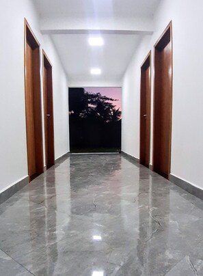 Un passadís amb un paviment de marbre polit, parets blanques i portes de fusta.