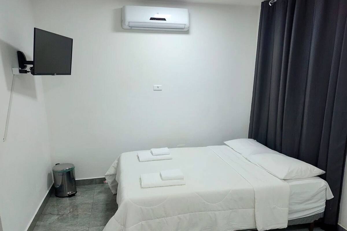 A small, clean room with a bed, a TV mounted on the wall, and a window with curtains.
