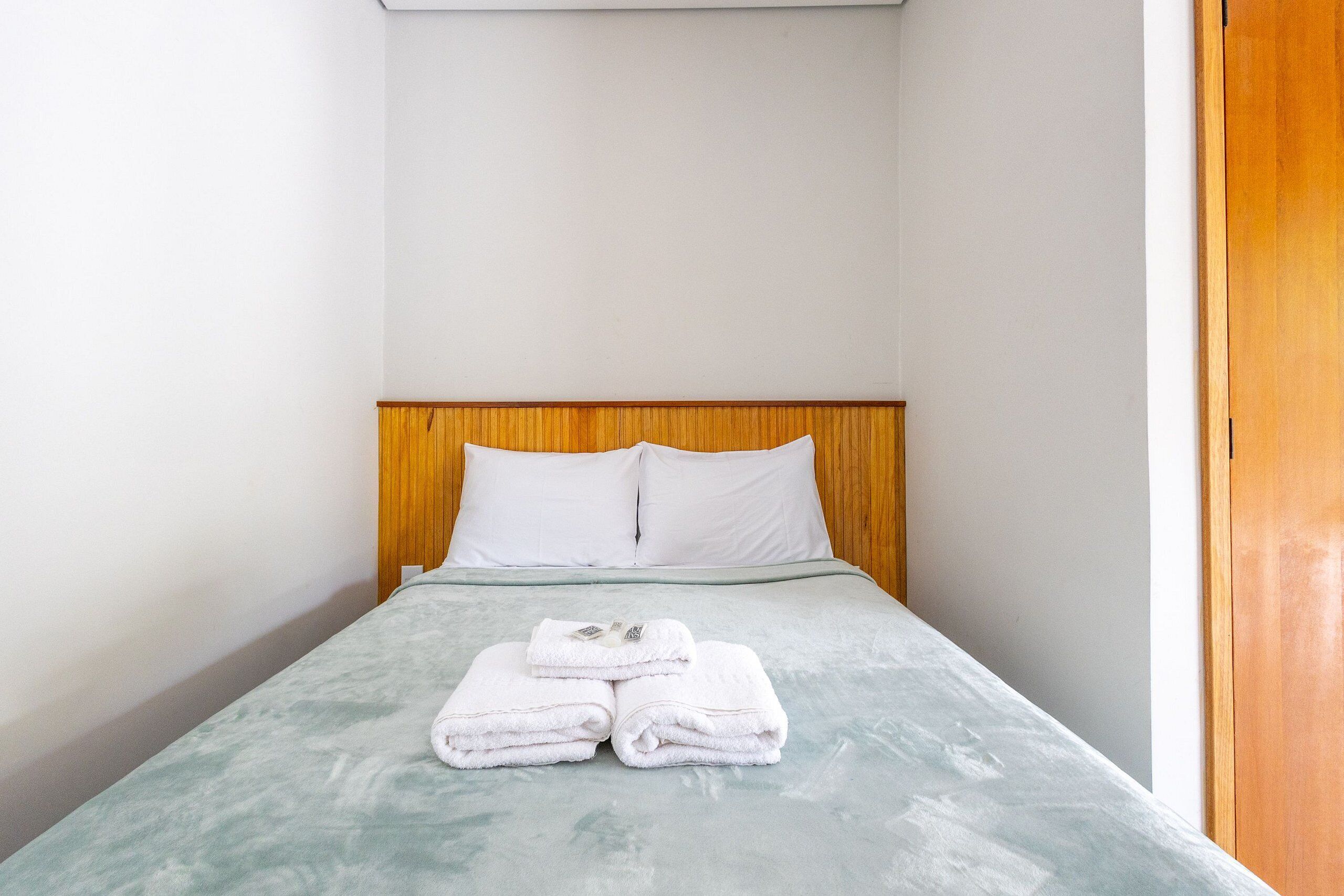 Un lit simple avec une tête de lit en bois, des oreillers blancs et une serviette blanche pliée posée sur le lit.