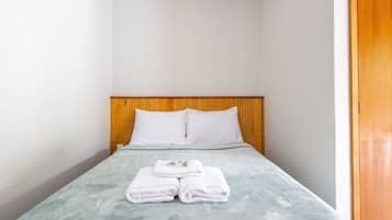 Una cama individual con cabecera de madera, almohadas blancas y una toalla blanca doblada sobre la cama.