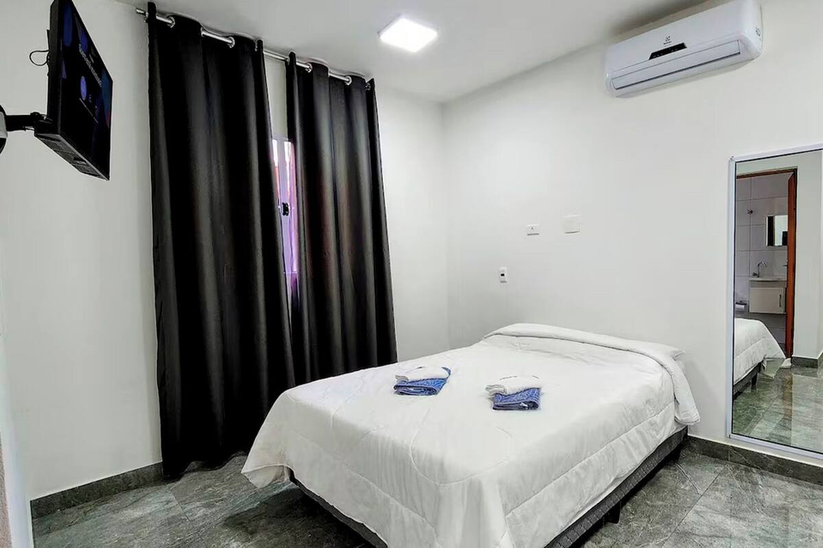 A hotel room with a bed, a mirror, an air conditioning unit, and a TV on the wall.