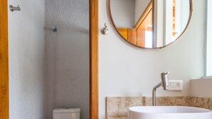 A bathroom with a white toilet, a sink with a marble countertop, and a wooden-framed mirror. - Maresias Suítes (São Sebastião)