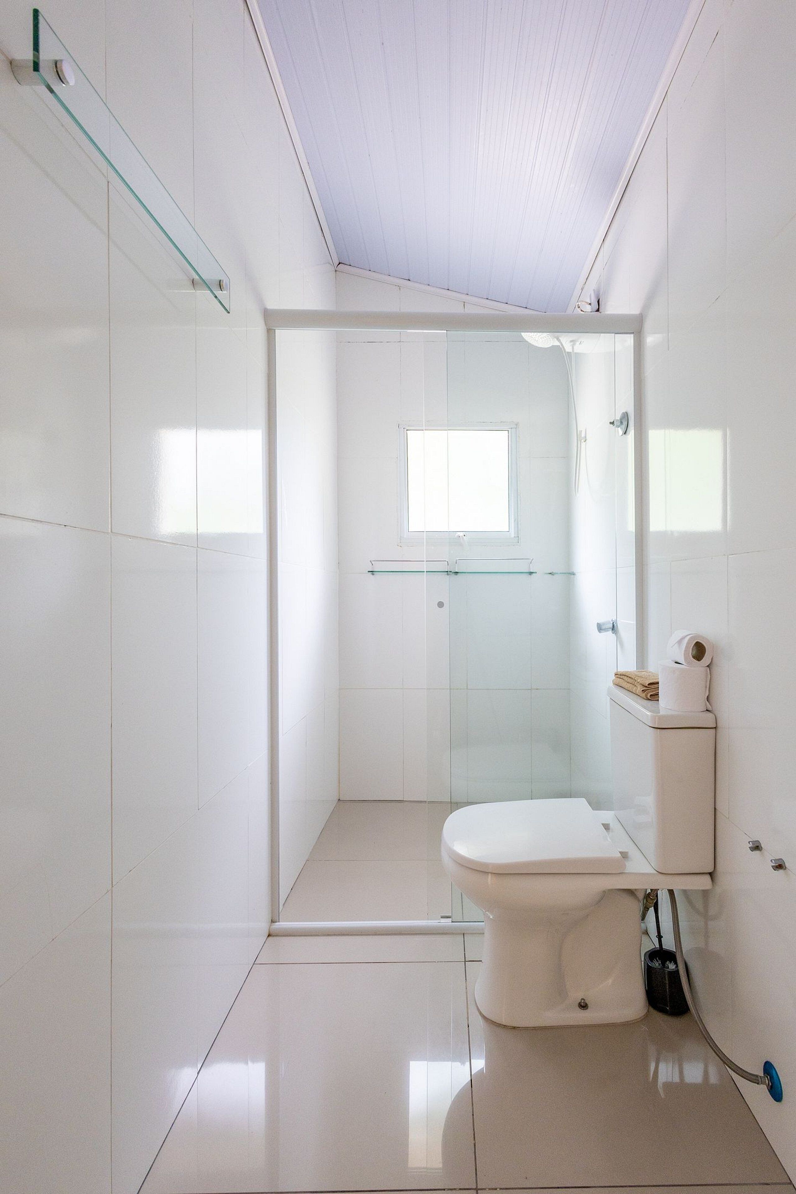 A modern bathroom with a toilet, a glass shower enclosure, and a small window.