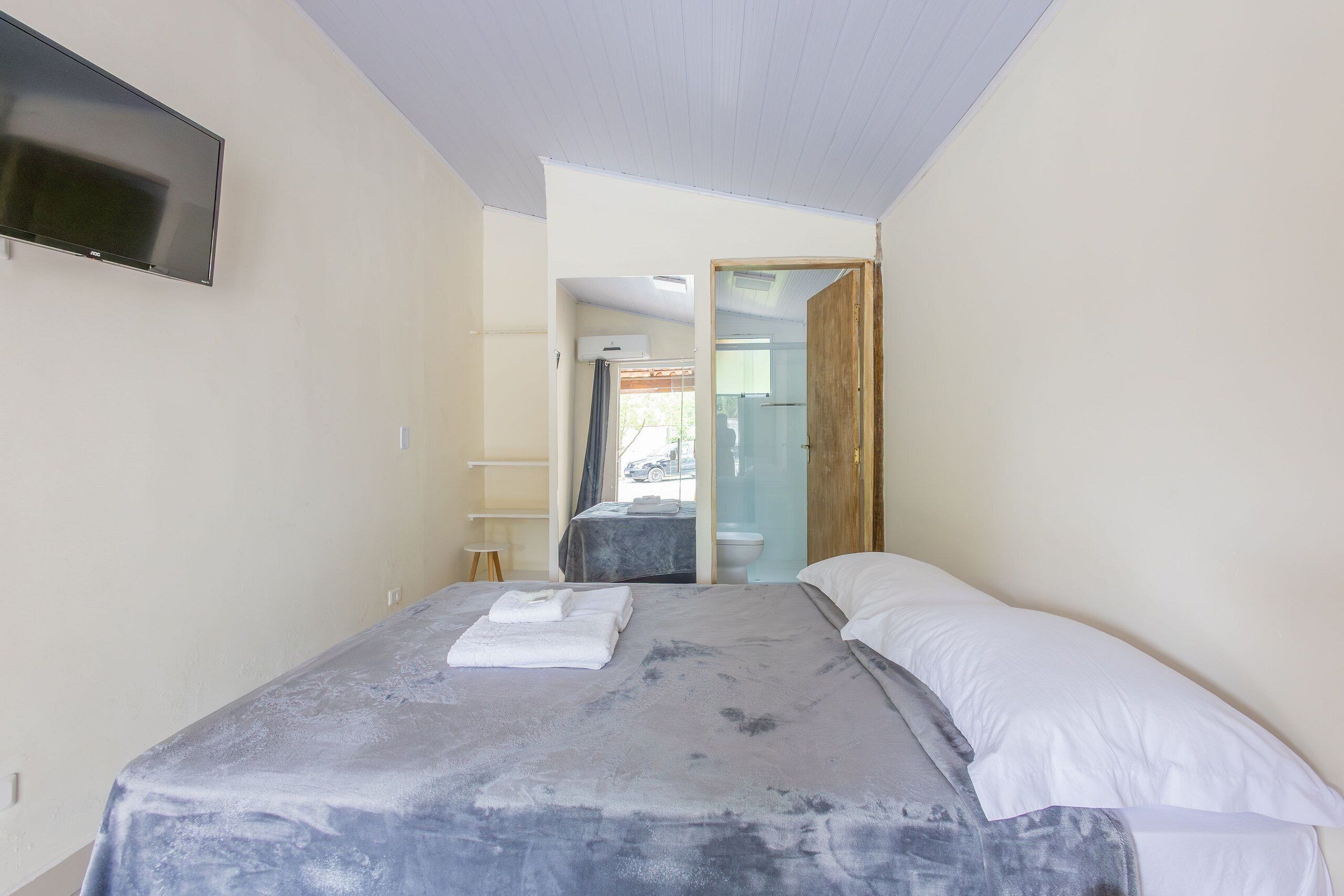 A bedroom with a bed, a TV mounted on the wall, and a bathroom visible through an open door.