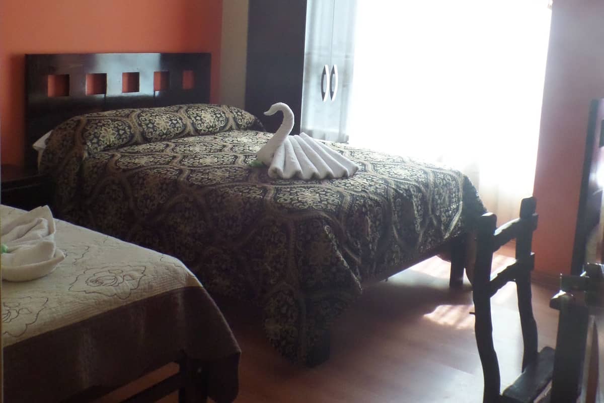 A bedroom with a large bed, a smaller bed, a wooden chair, a wardrobe, and a window with curtains.
