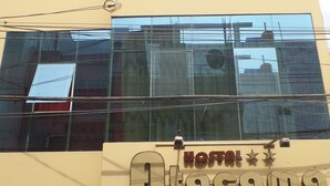 A hotel facade with the name 'Atacama' prominently displayed. There are multiple windows, some with curtains, and a visible elevator. The building has a modern architectural style with a beige and blue color scheme. - HOSTAL ATACAMA (Tacna)