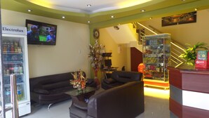 A lobby with a refrigerator stocked with beverages, a sofa, a coffee table with a vase, and a counter with snacks. - HOSTAL ATACAMA (Tacna)