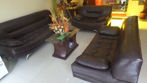 A living room with a dark brown sofa set, a glass coffee table with a decorative centerpiece, and a leather armchair. - HOSTAL ATACAMA (Tacna)