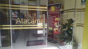 A hotel entrance with a glass door, a welcome mat, and a poster detailing services like private rooms, cable TV, and internet. - HOSTAL ATACAMA (Tacna)