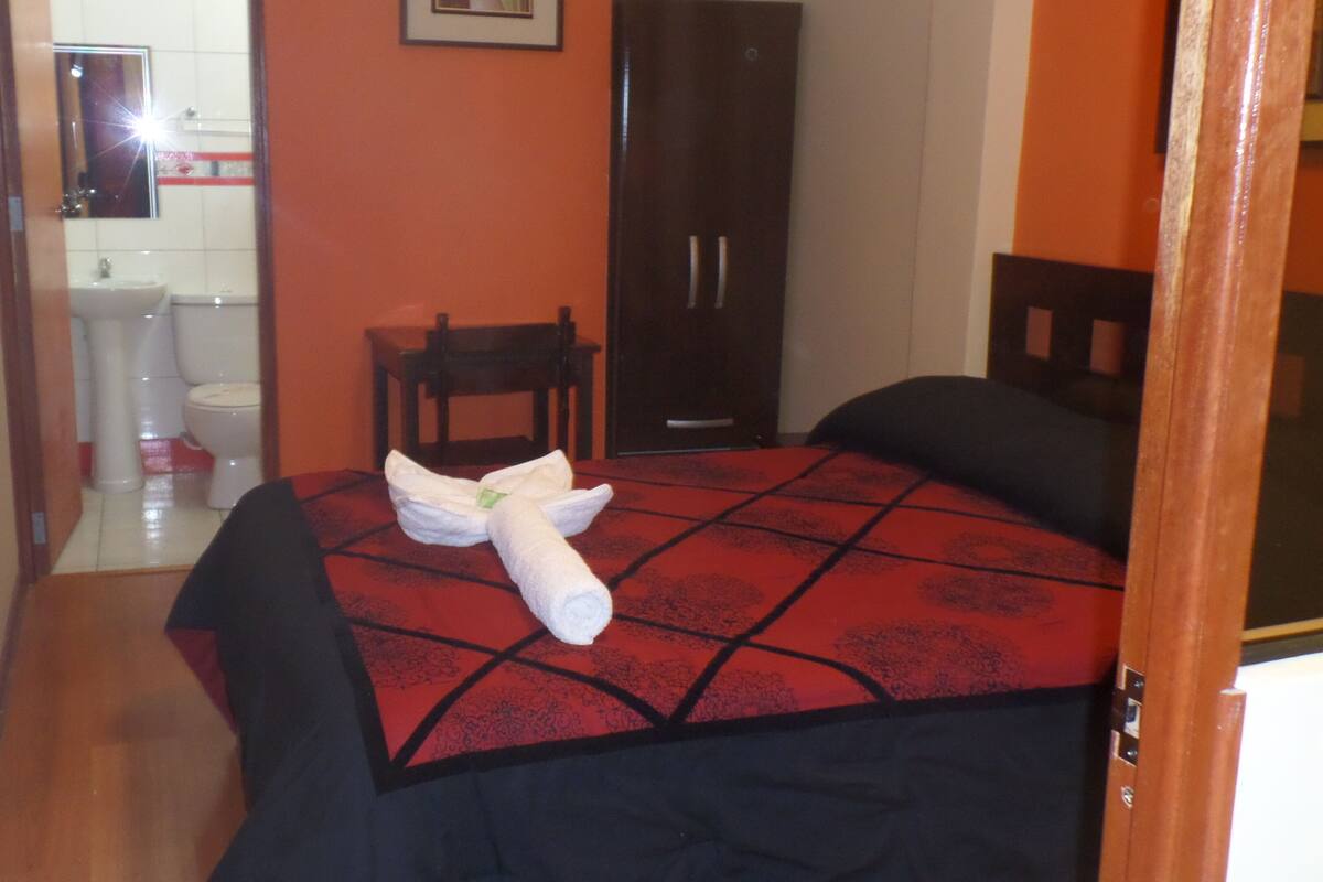 A hotel room with a bed, a chair, a wardrobe, and a bathroom visible through an open door.