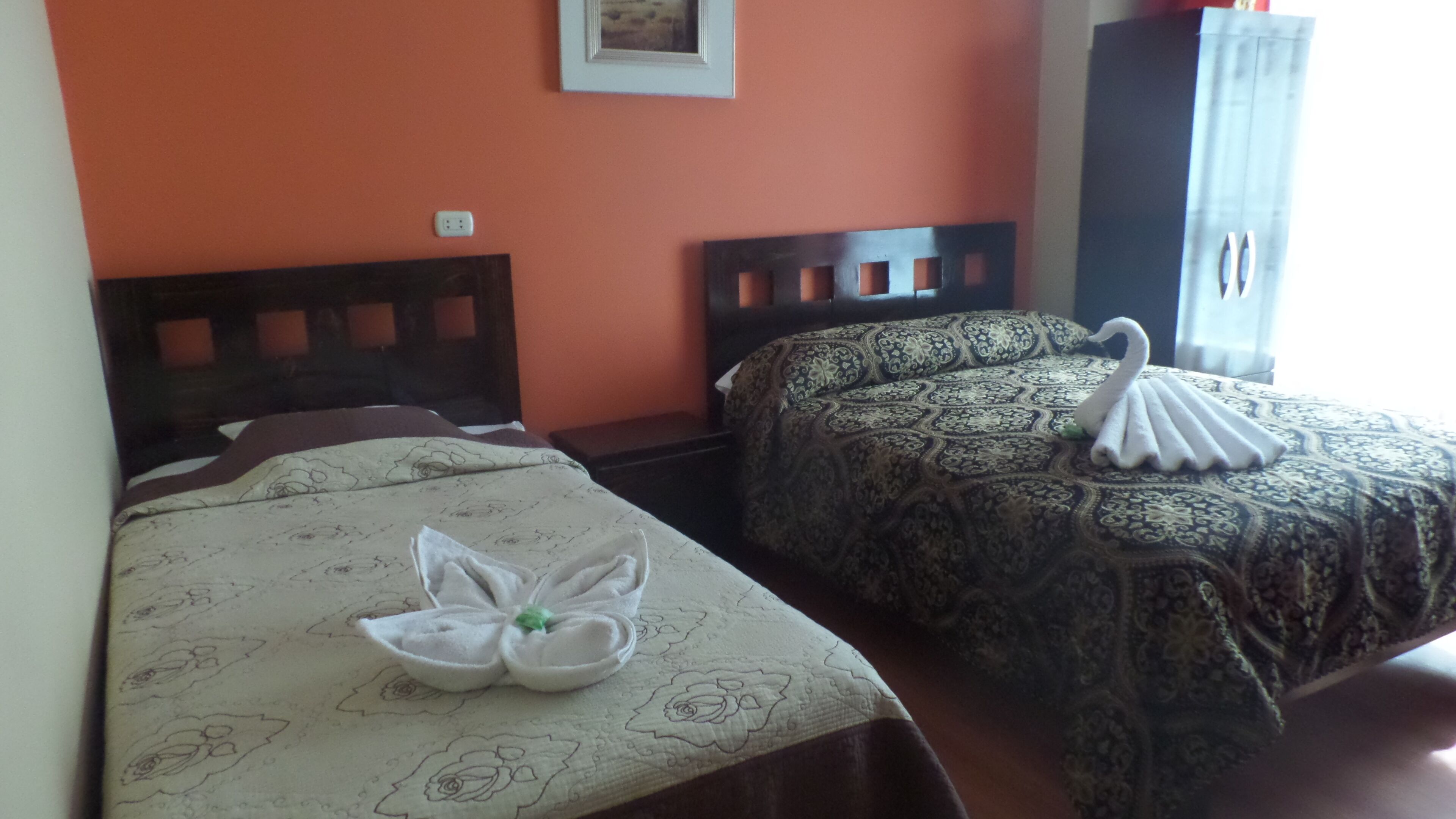 Dos camas individuales con ropa de cama estampada con motivos florales, un cabecero de madera y una toalla con forma de cisne en la cama de la izquierda.