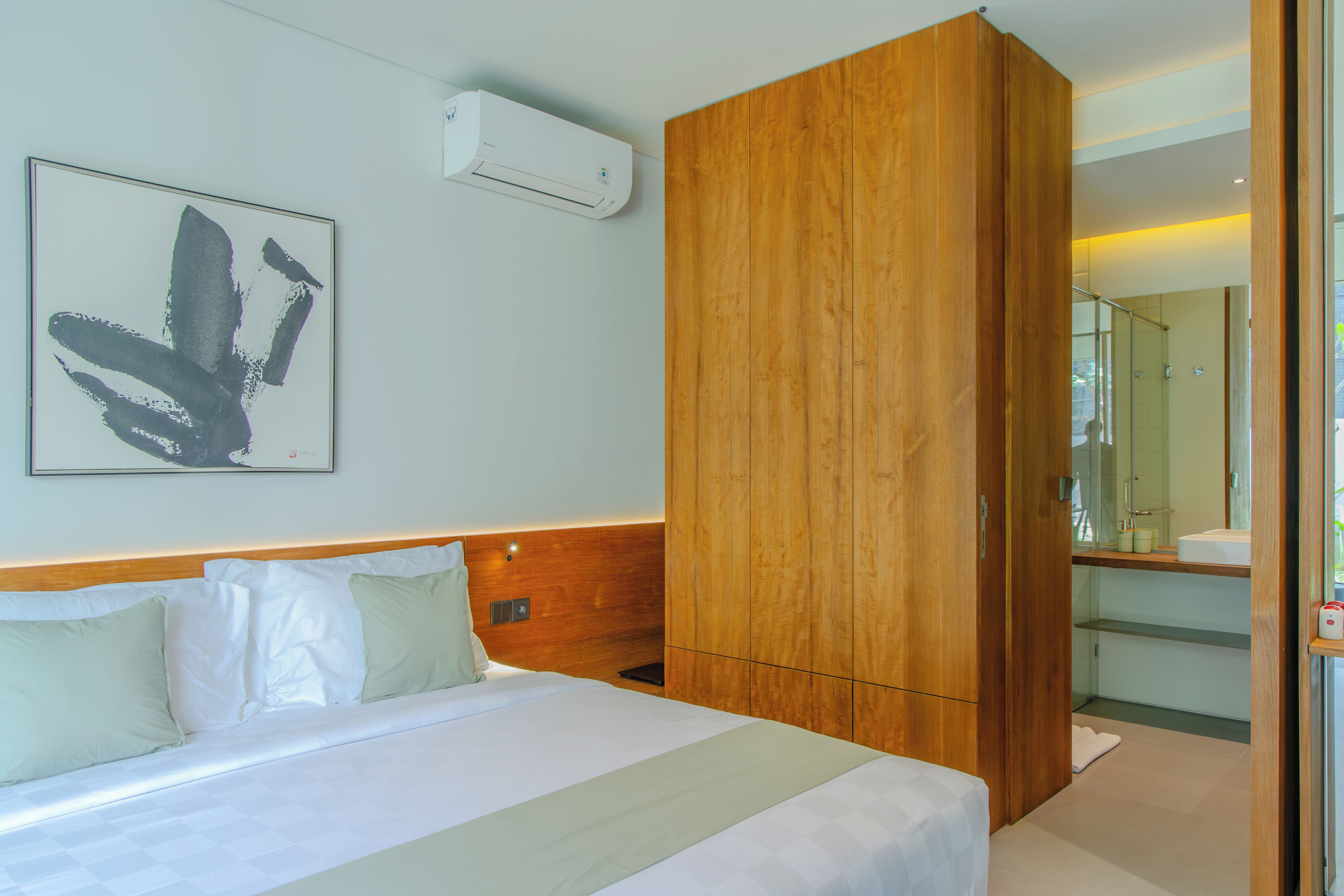 A modern hotel room with a large bed, a wooden wardrobe, a wall-mounted air conditioner, and a bathroom visible through an open door.