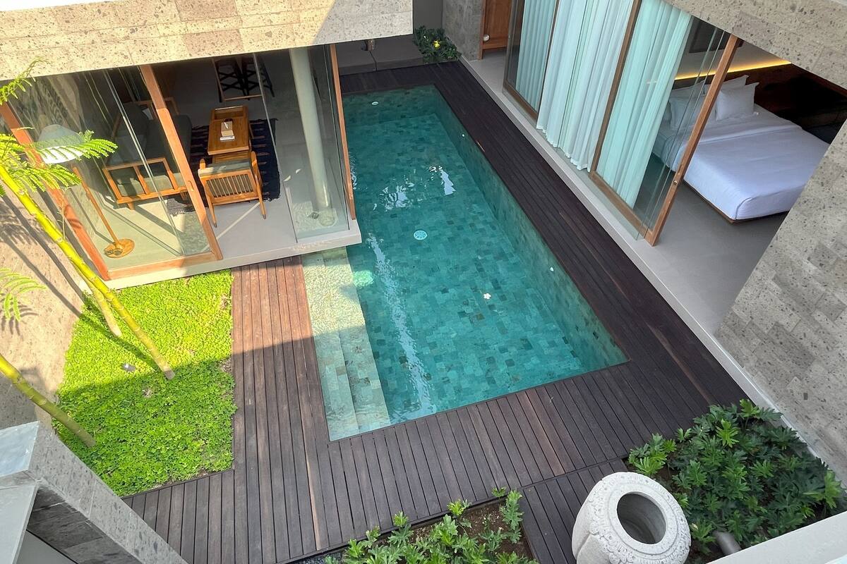 A modern outdoor pool area with a wooden deck, a glass-enclosed lounge, and a view of the pool.