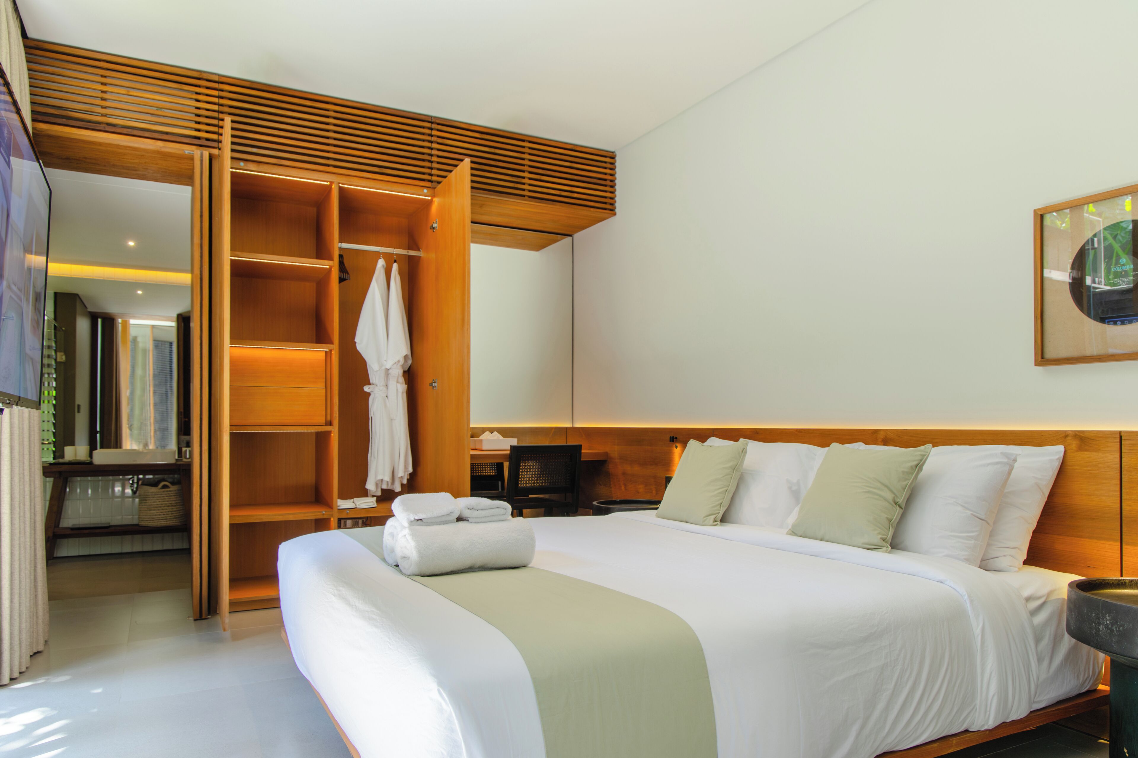 A hotel room with a large bed, a wooden wardrobe, a desk, and a bathroom visible through an open door.