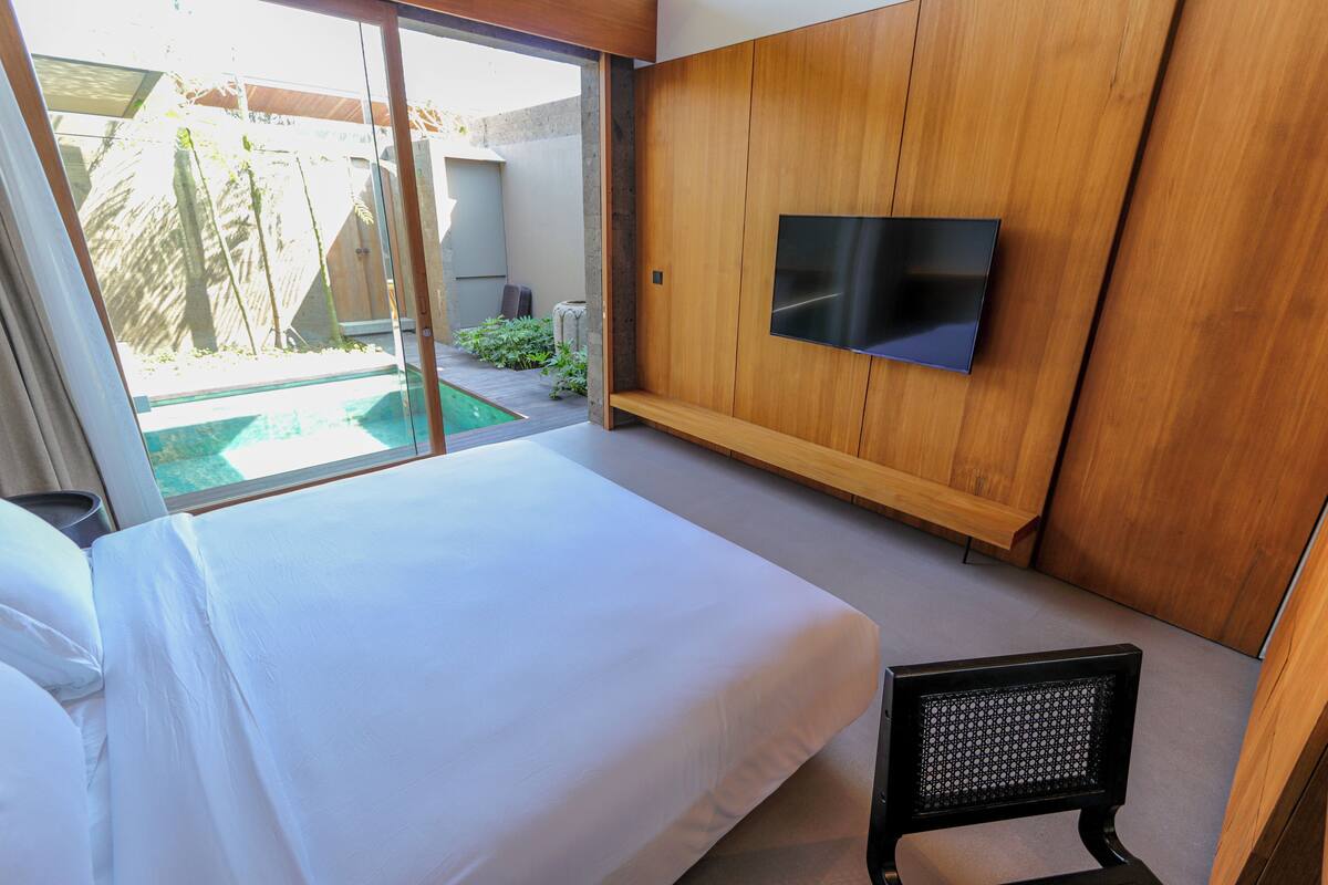 A modern hotel room with a large bed, a TV mounted on the wall, and a view of a swimming pool.